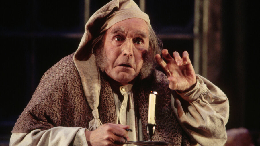 Ebenezer Scrooge holds a candle stick.
